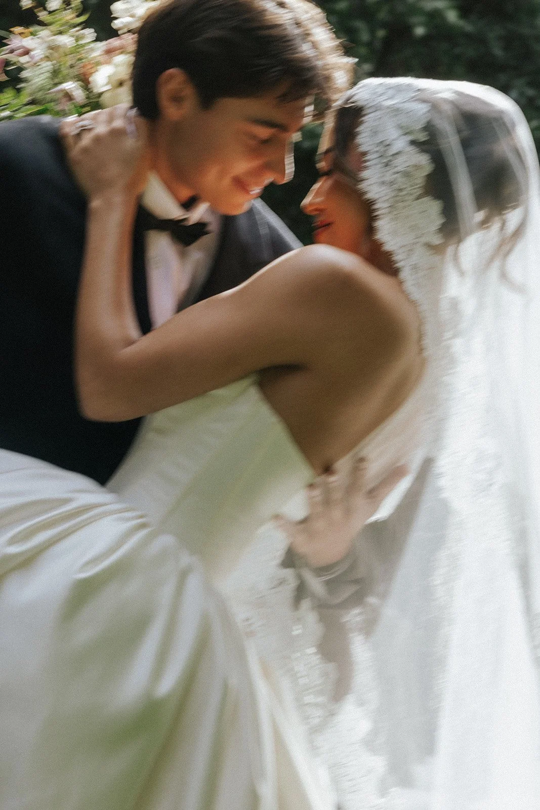 A bride and groom sharing an intimate moment during their wedding, with the groom in a tuxedo and the bride in a white dress with a veil.