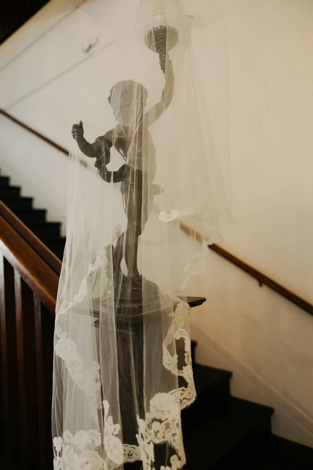A staircase with a wooden handrail and a decorative statue of a girl in a dress holding a basket, shrouded by a sheer lace curtain.