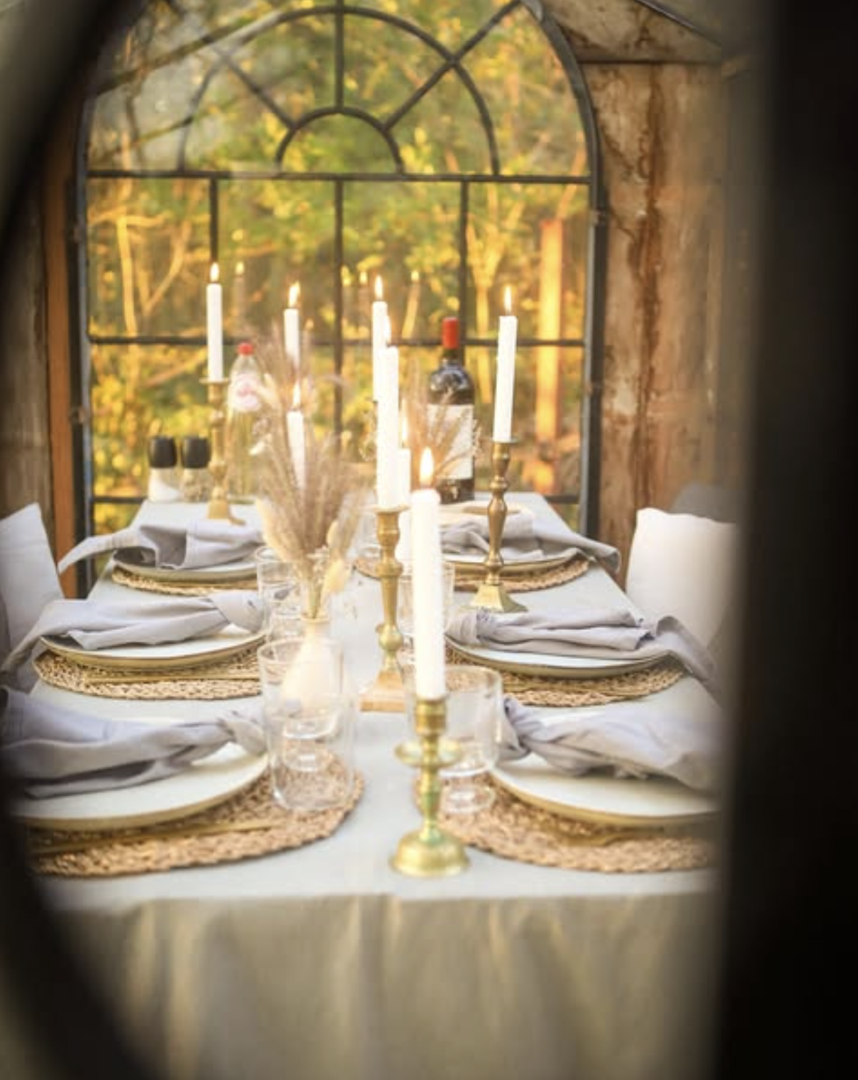 Long table with tall candles and an arched window inside La Roulotte, glimpsed through a round opening.