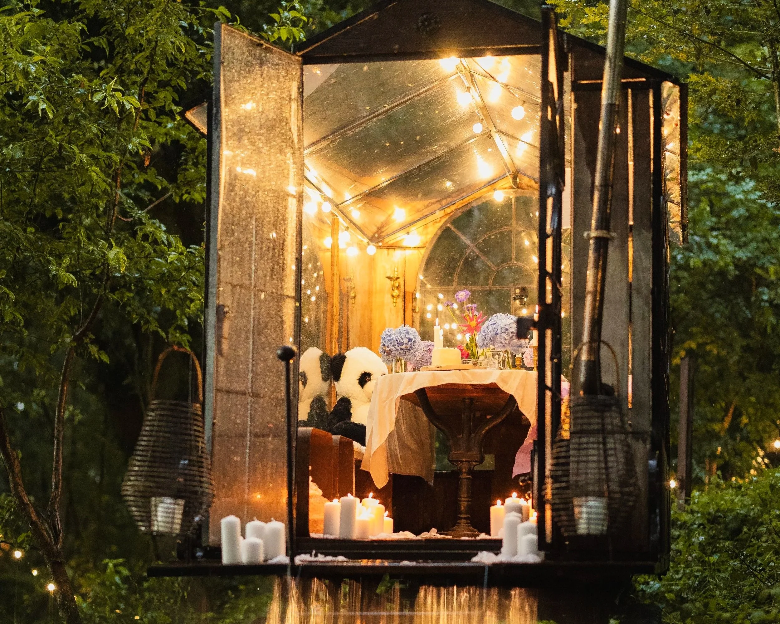 La Roulotte at night with its doors wide open, candles at the entrance and string lights glowing inside.