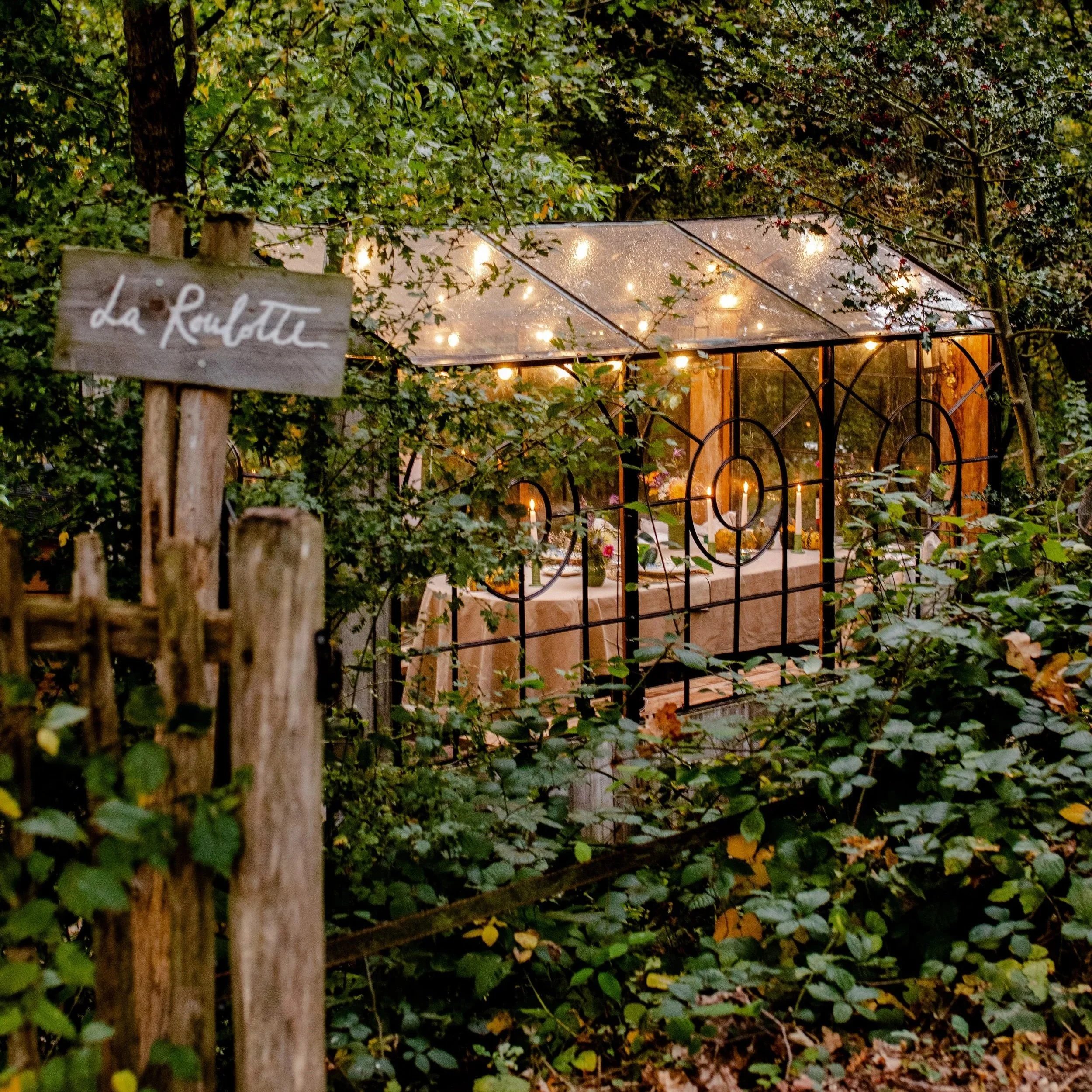 Candlelit table set for a private dinner inside La Roulotte, a glass cabin in the forest.