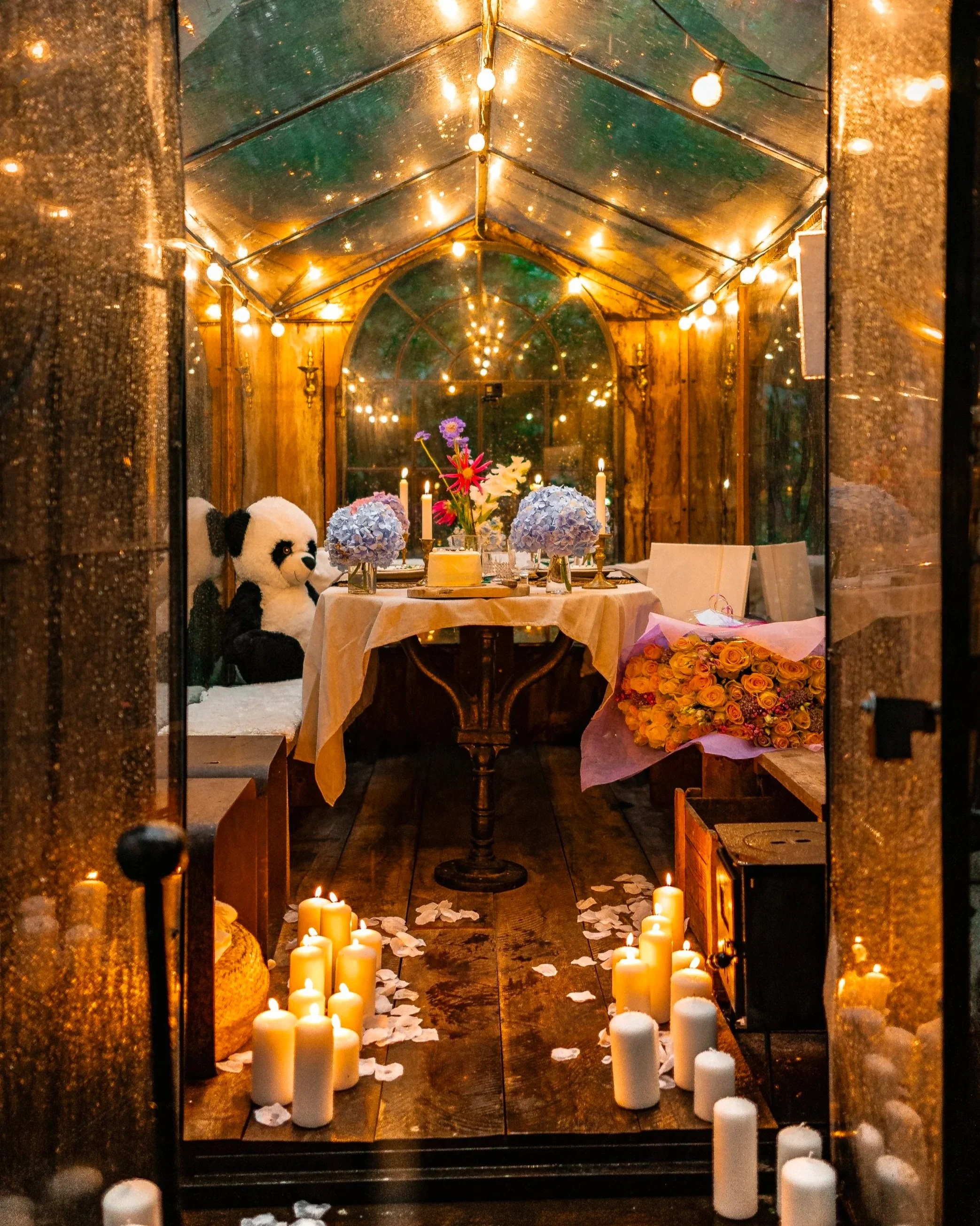 Candlelit path leading to a flower-decked table inside La Roulotte, glowing with string lights at night.