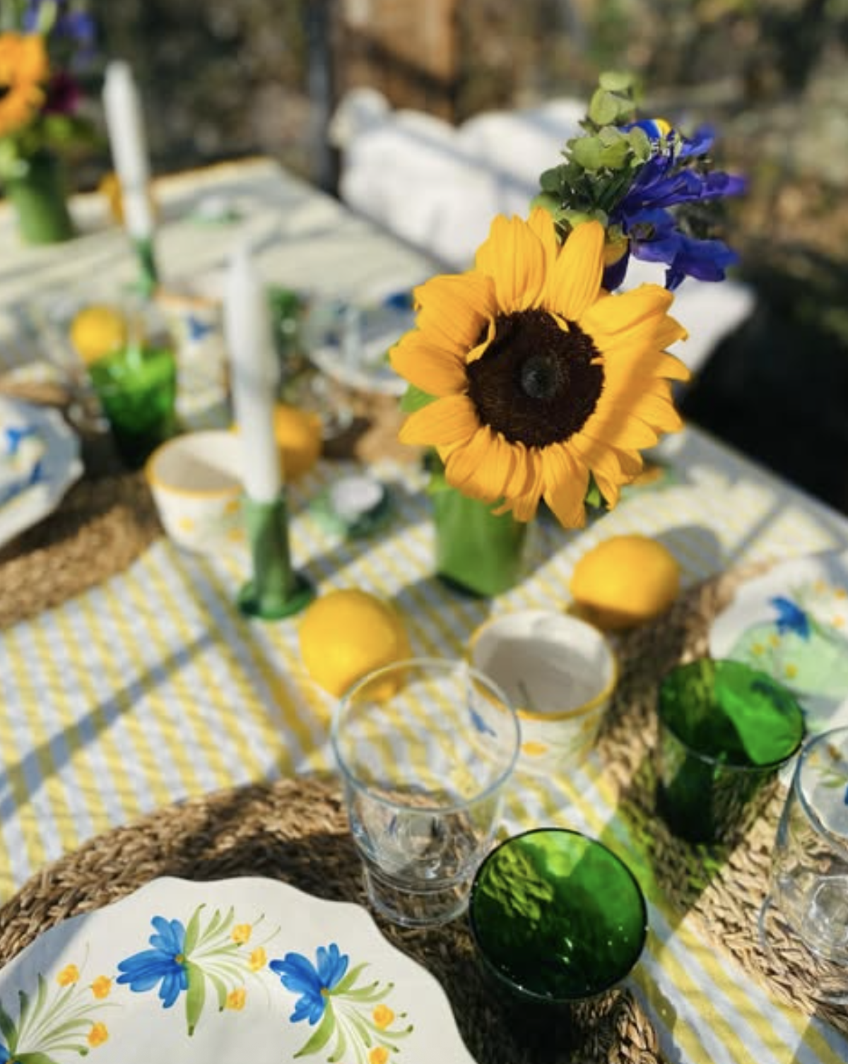 Sunny summer table with sunflowers, green glasses and blue floral plates.