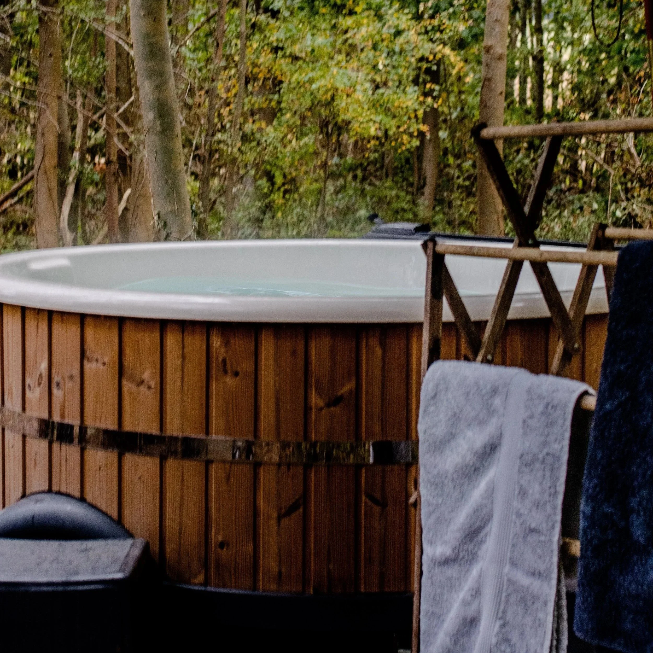 Wood-fired spa on a wooden deck in the forest, with towels ready for guests.