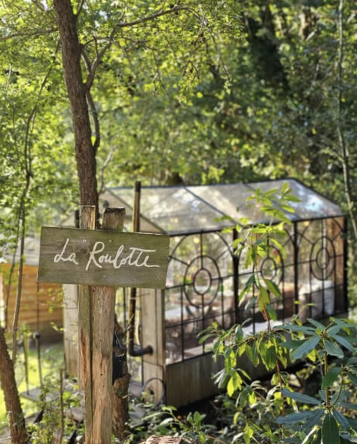 La Roulotte wooden sign beside the glass cabin, hidden among the trees in the forest.