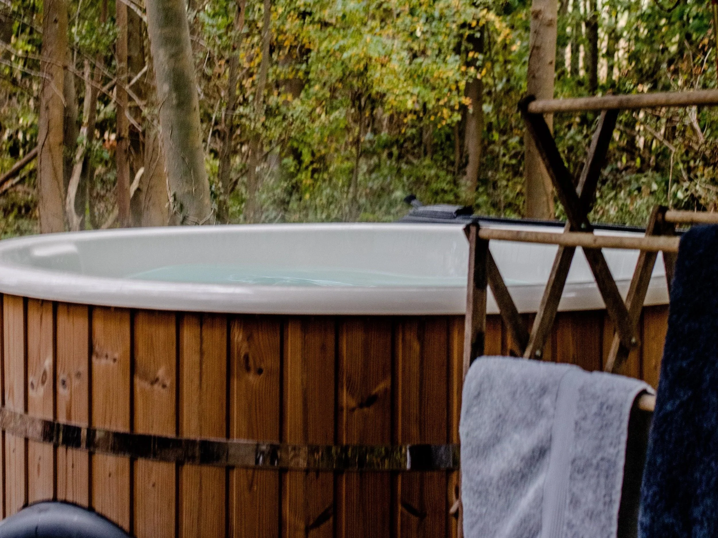 Close-up of the wood-fired hot tub with a fresh towel on the rack, surrounded by forest.