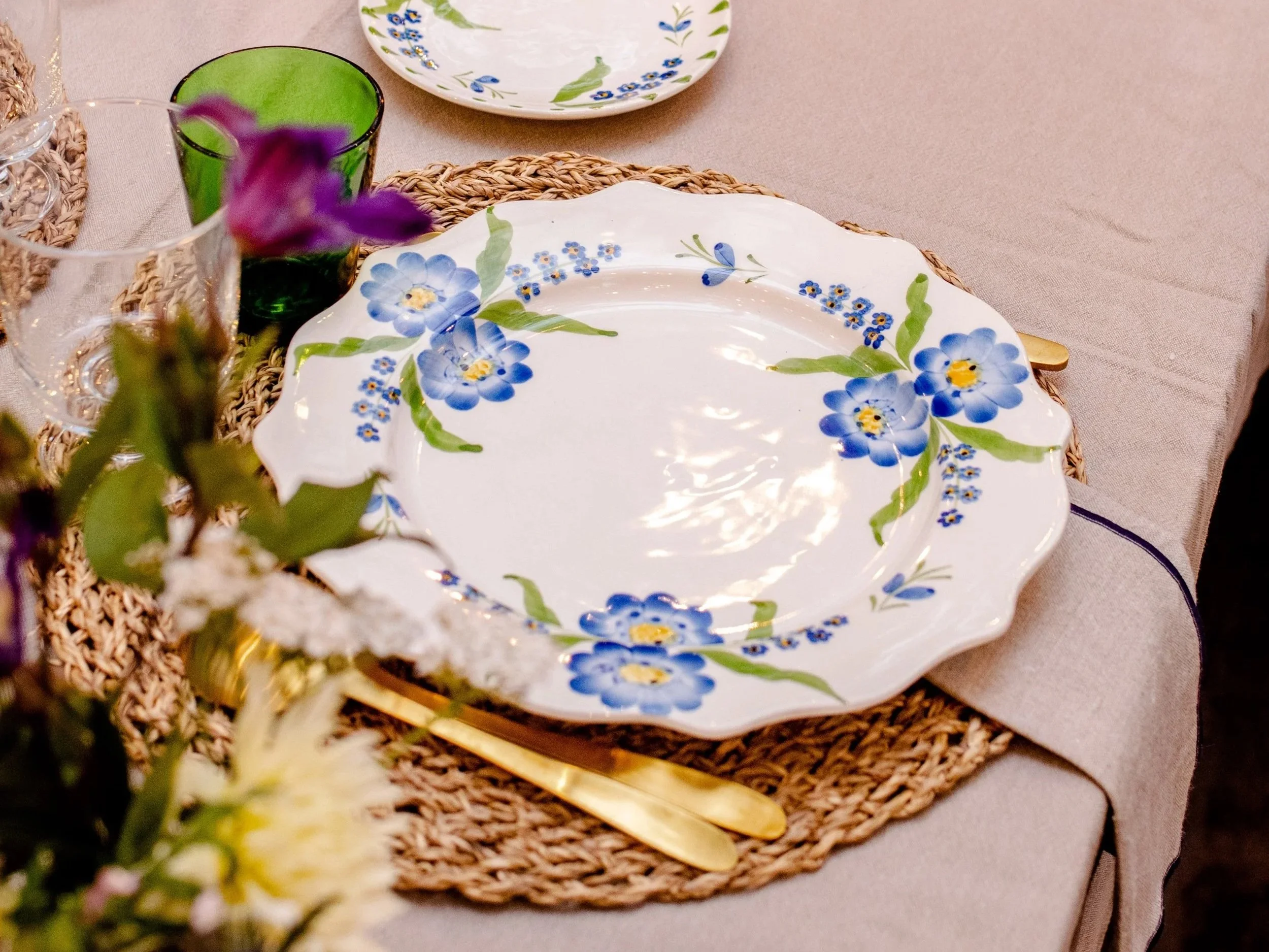 Hand-painted blue floral plate with gold cutlery and fresh flowers, part of the table setting at La Roulotte.