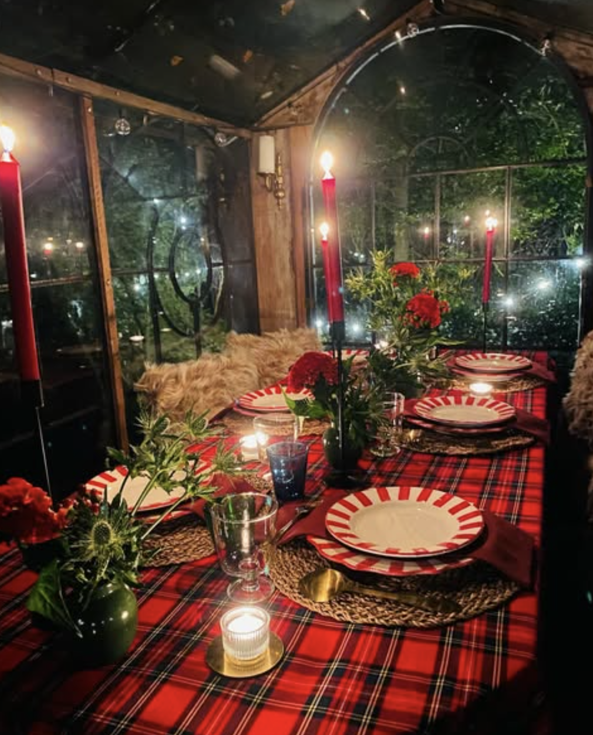 Festive table with a red tartan tablecloth, candles and red flowers inside La Roulotte at night.