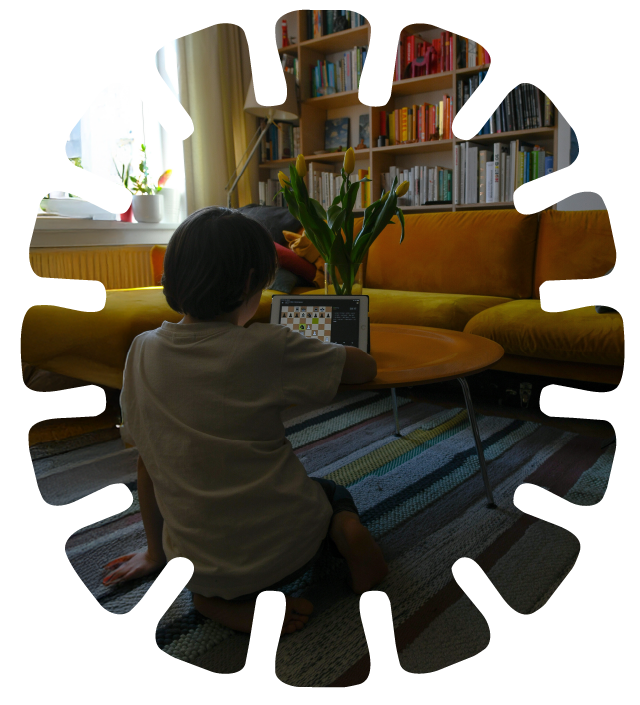 Child sitting on a striped rug, playing chess on a tablet in a cozy living room with a yellow sofa, a wooden coffee table, a bookshelf, and a window with yellow curtains and a flowerpot.