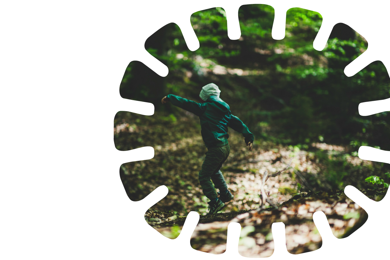 Child skipping along a forest trail surrounded by green trees.