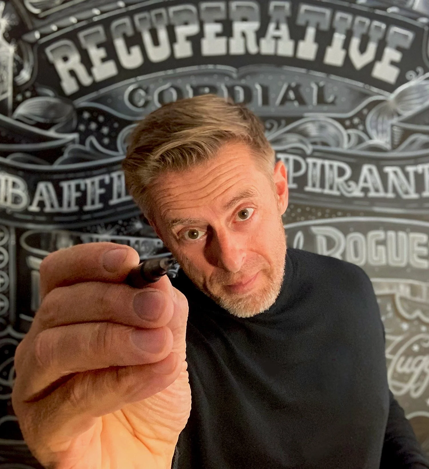 Vic Lee holding a drawing pen in front of one of his hand-painted typography murals