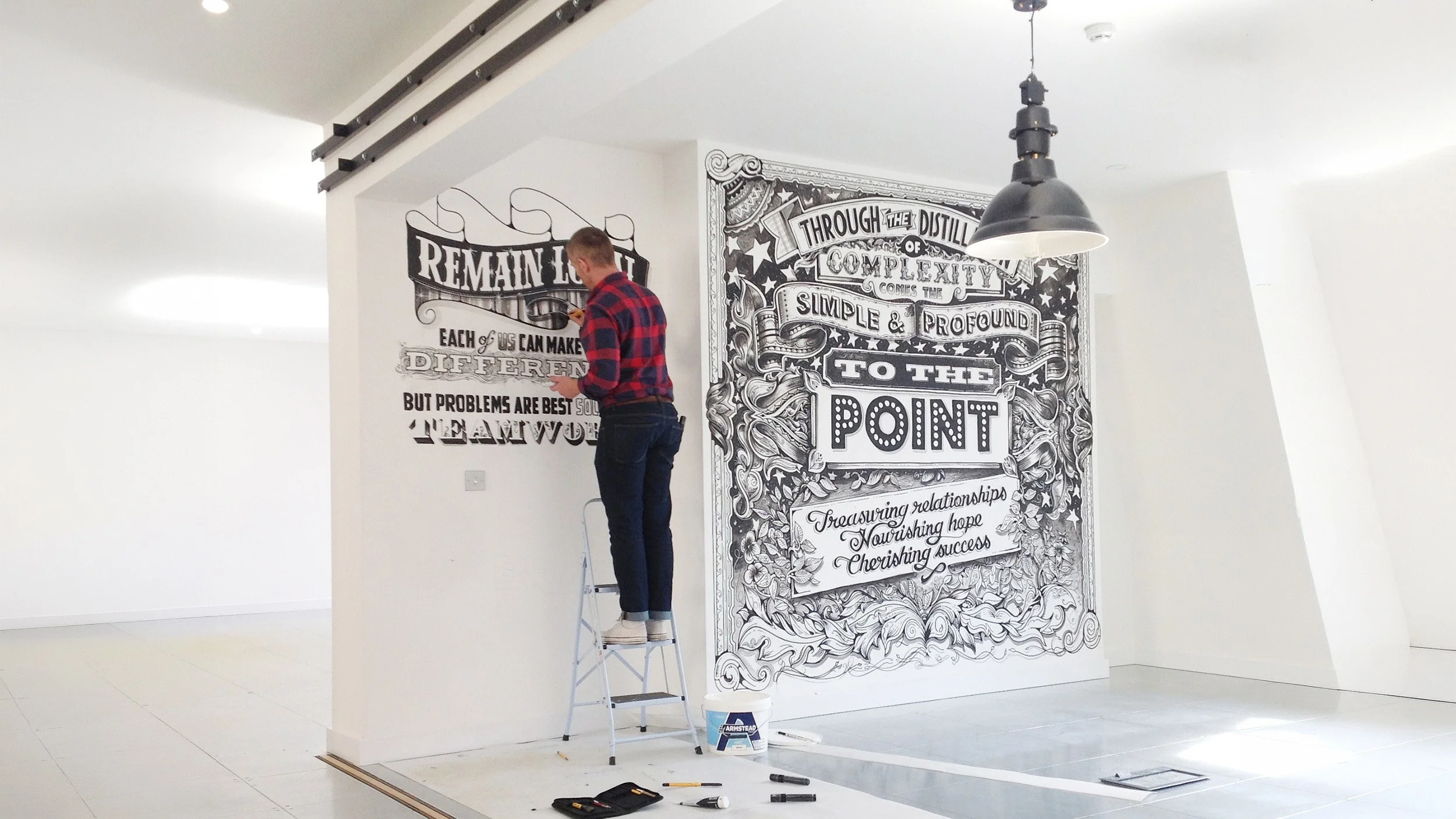 Vic Lee hand-painting a black and white typographic mural inside a contemporary interior space.