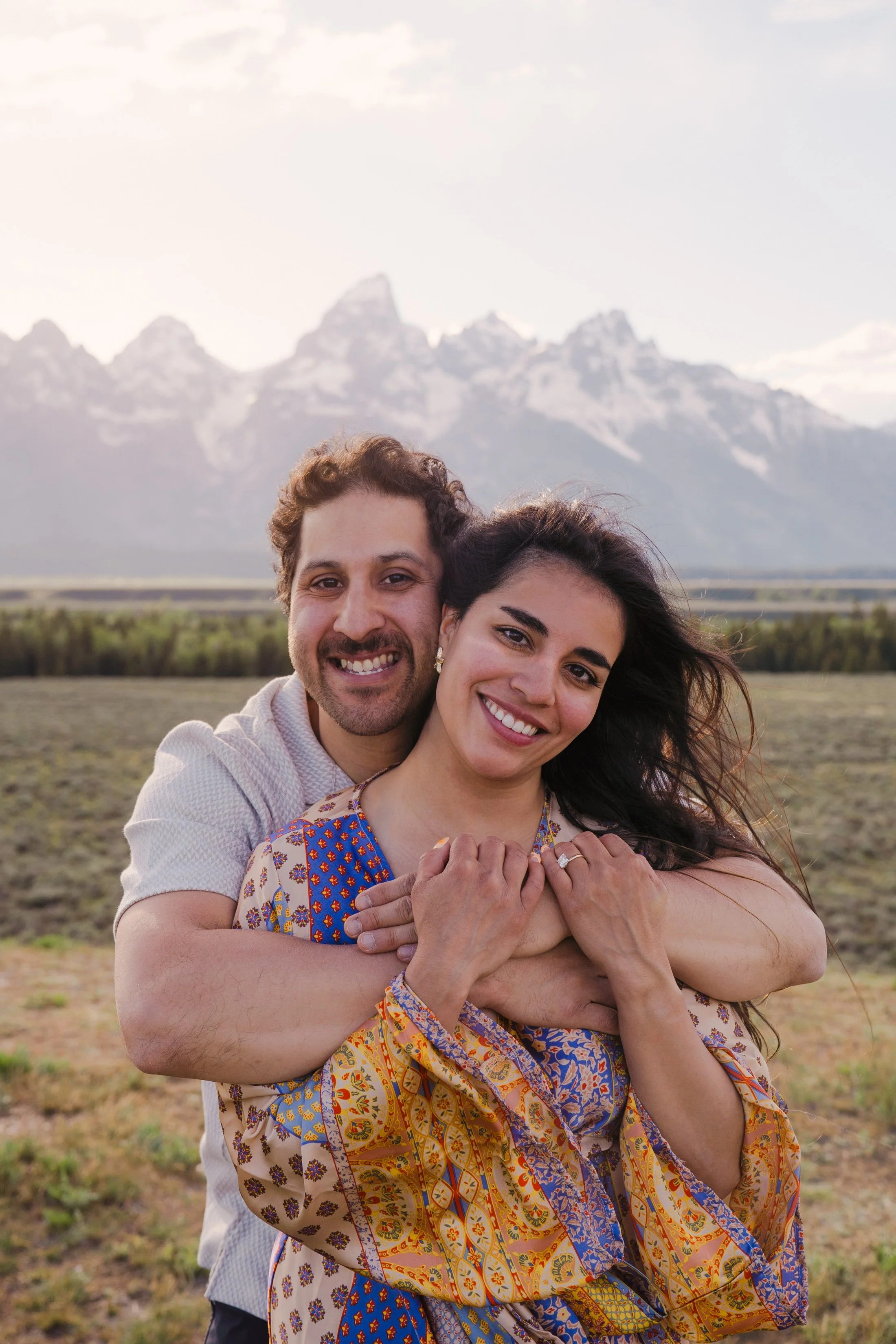 A couple smiling and embracing with at Glacier View Turnout in Grand Teton National Park.