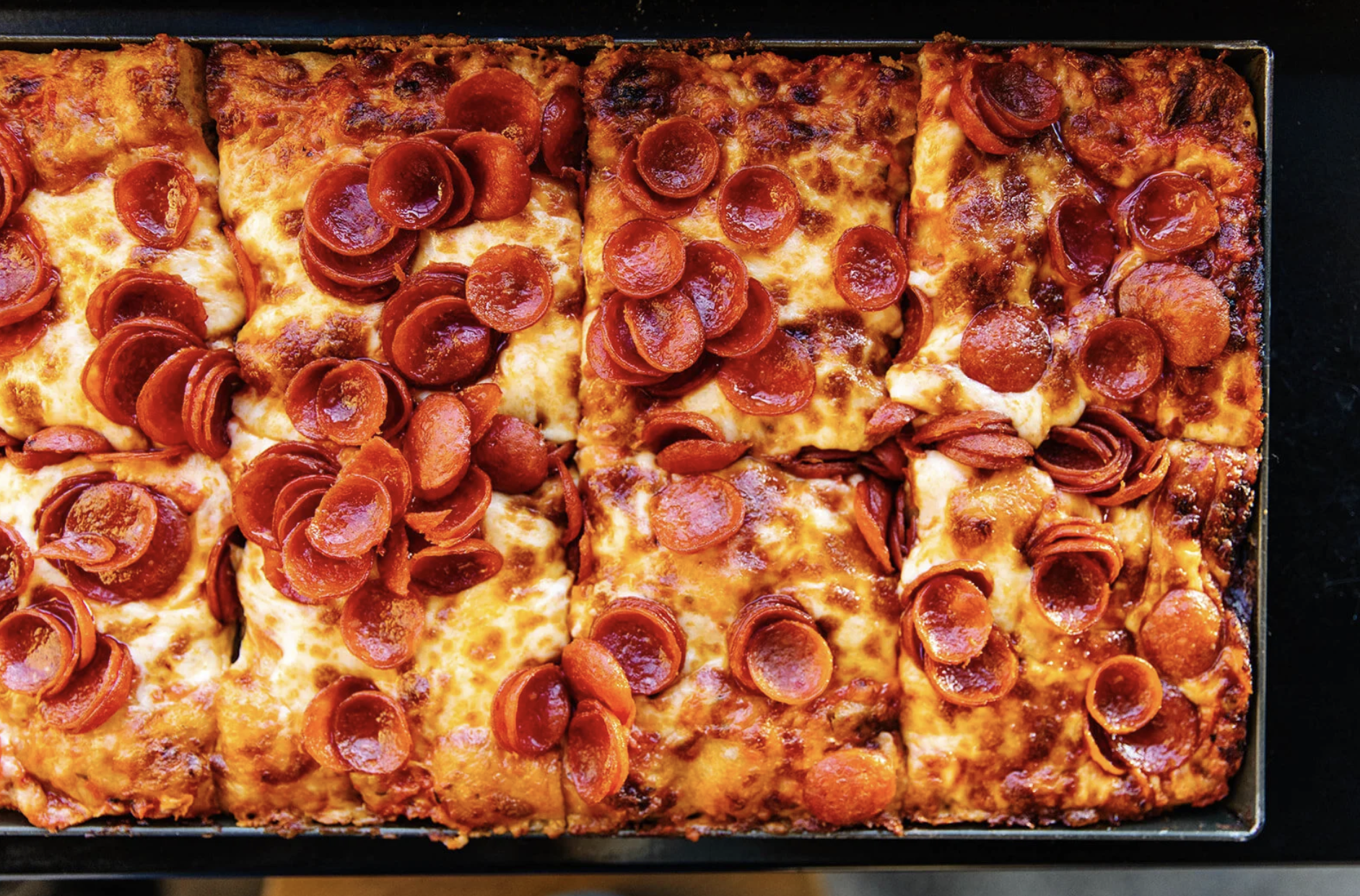 Close-up of our pan-baked, Detroit-ish style pizza with melted cheese and cup-and-char pepperoni, baked to a golden brown, with some slightly burnt edges.