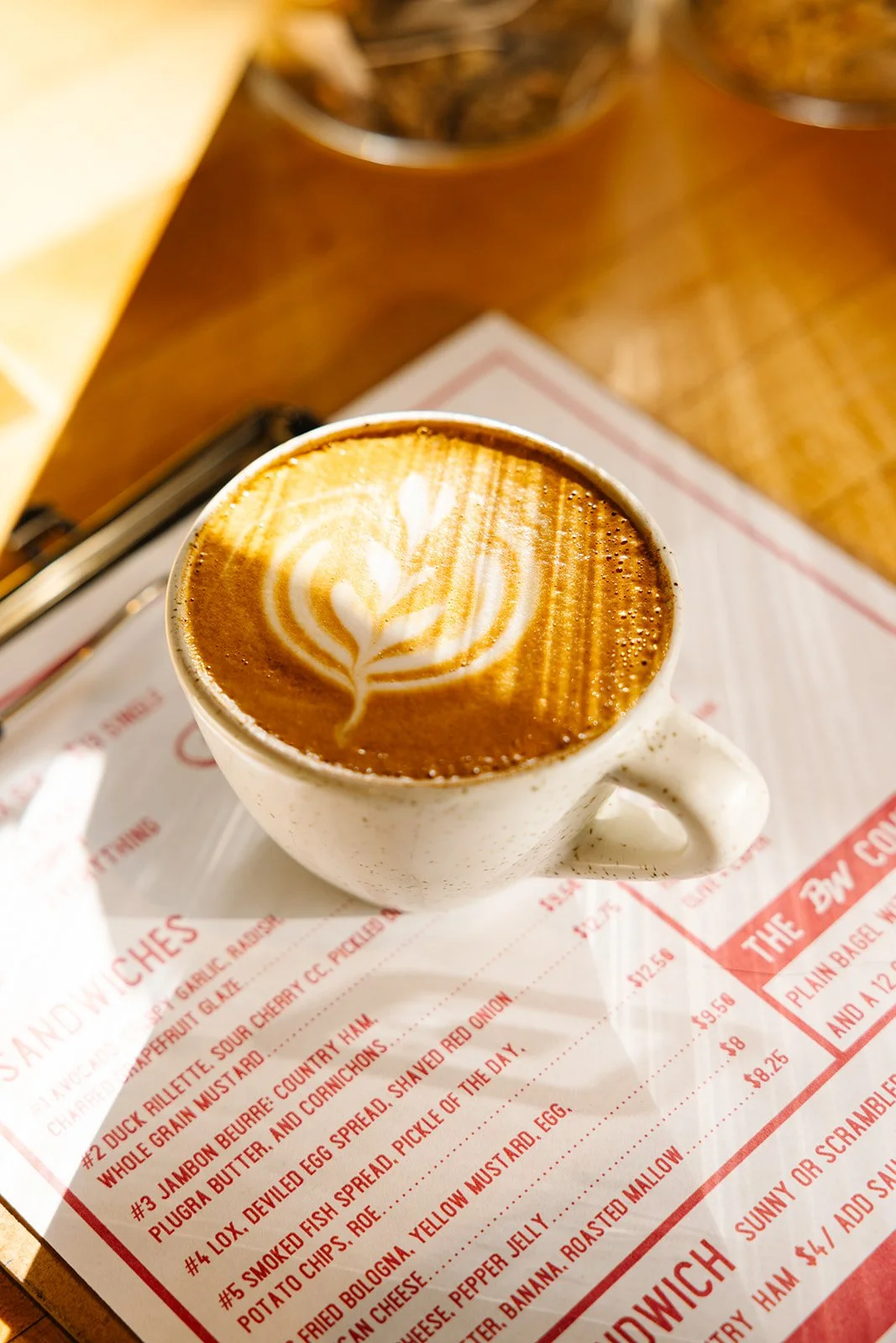 A cup of coffee with latte art on top, placed on a paper menu on a wooden table.