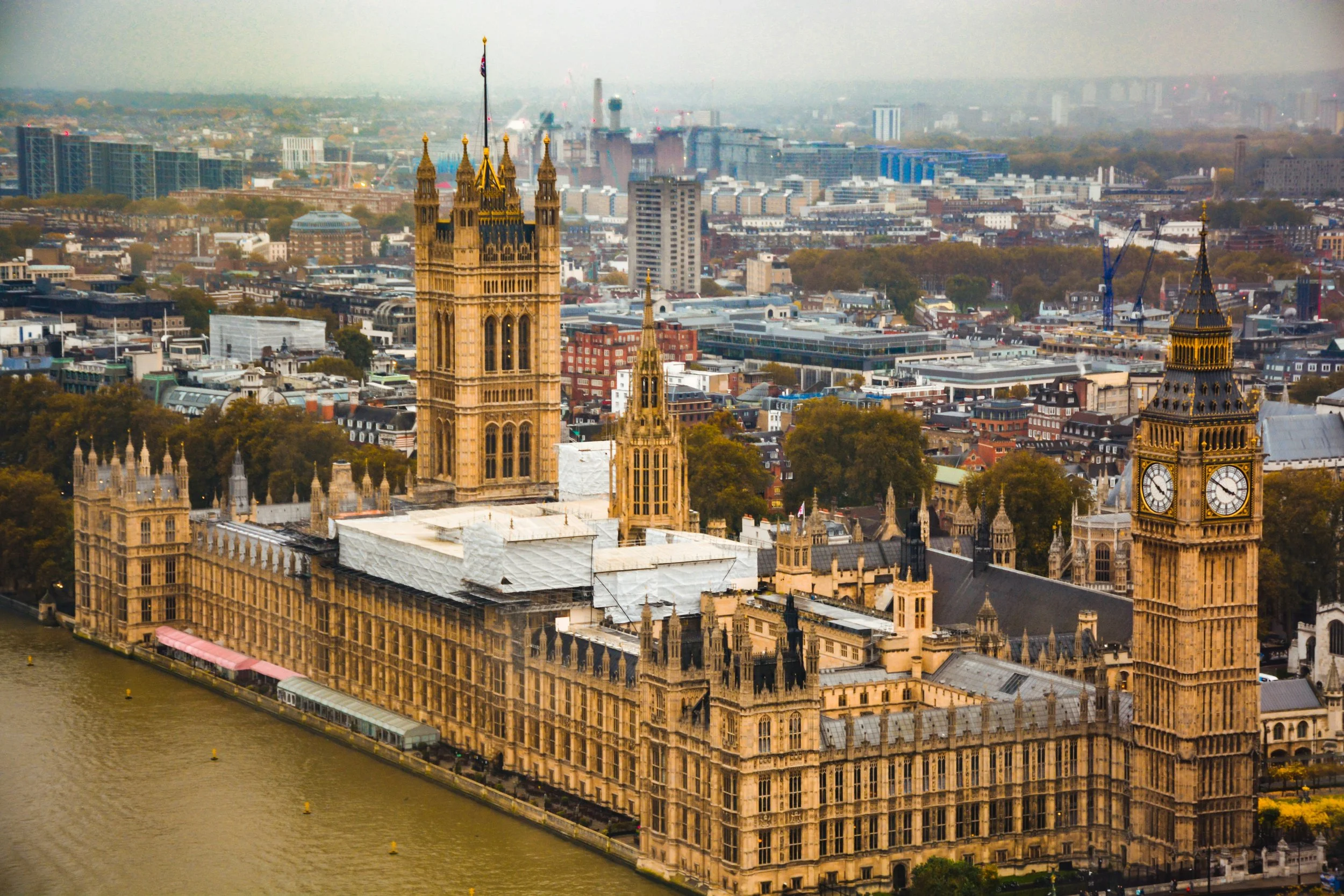 Aerial view of the Palace of Westminster and Big Ben clock tower in London, with city buildings and distant skyline.