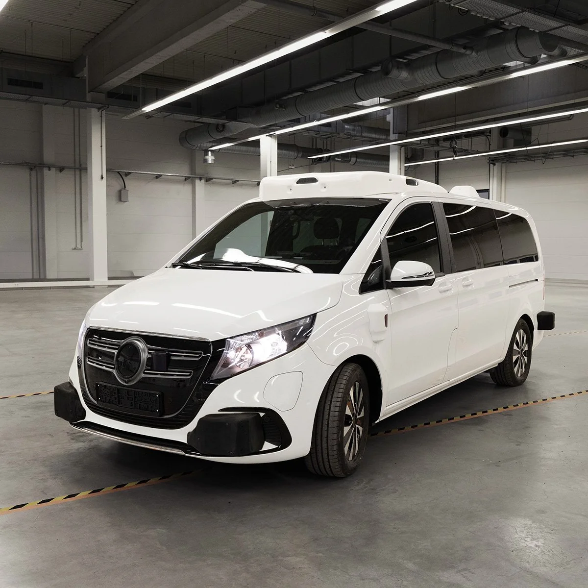 White autonomous vehicle with black front grille and shield logo, parked in an indoor garage.