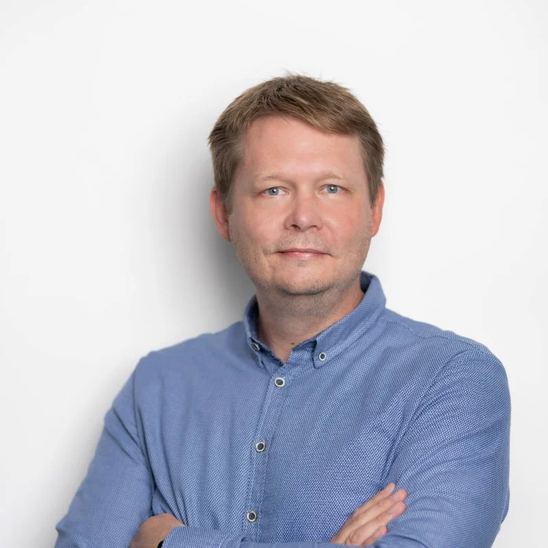A man in a blue button-up shirt standing against a white background.