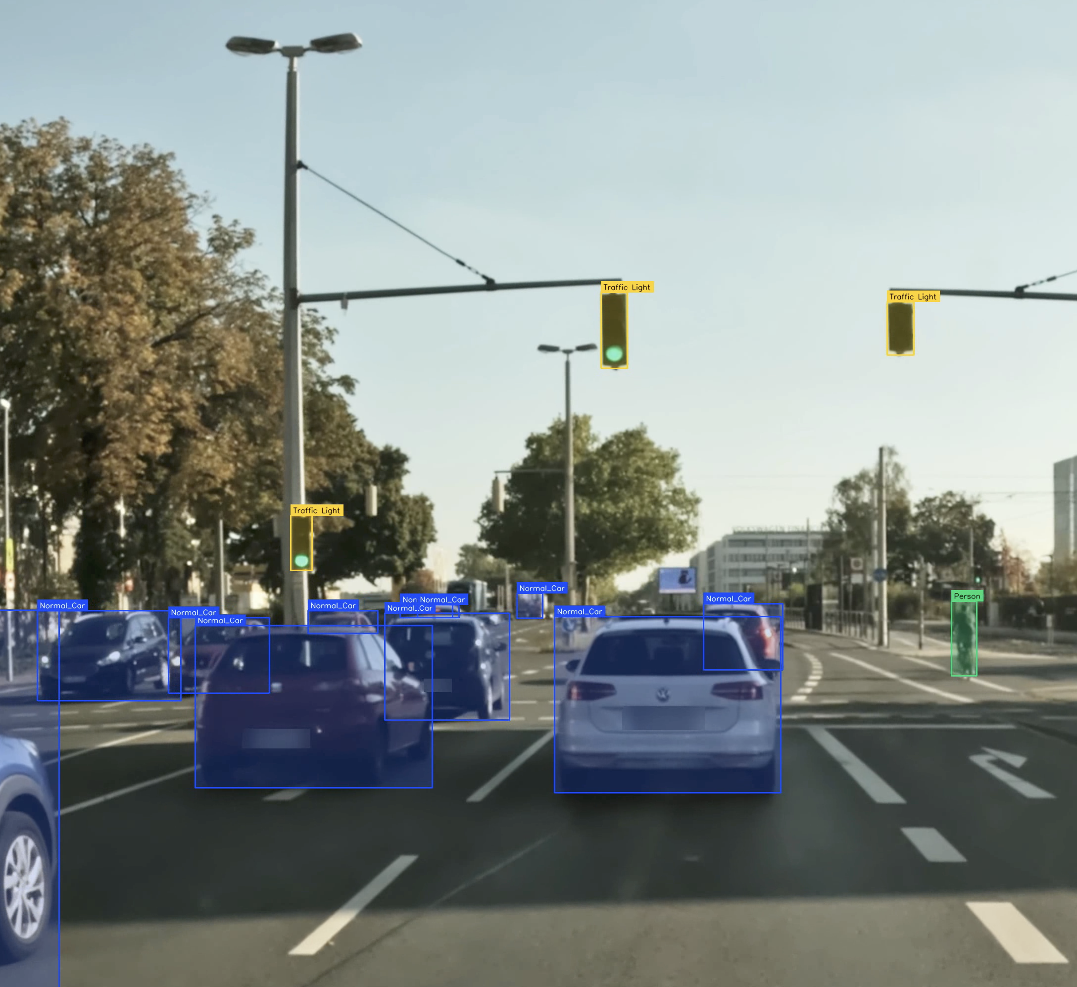 Traffic lights with green signals on a busy street, cars stopped at the intersection, trees and buildings in the background, in daytime.