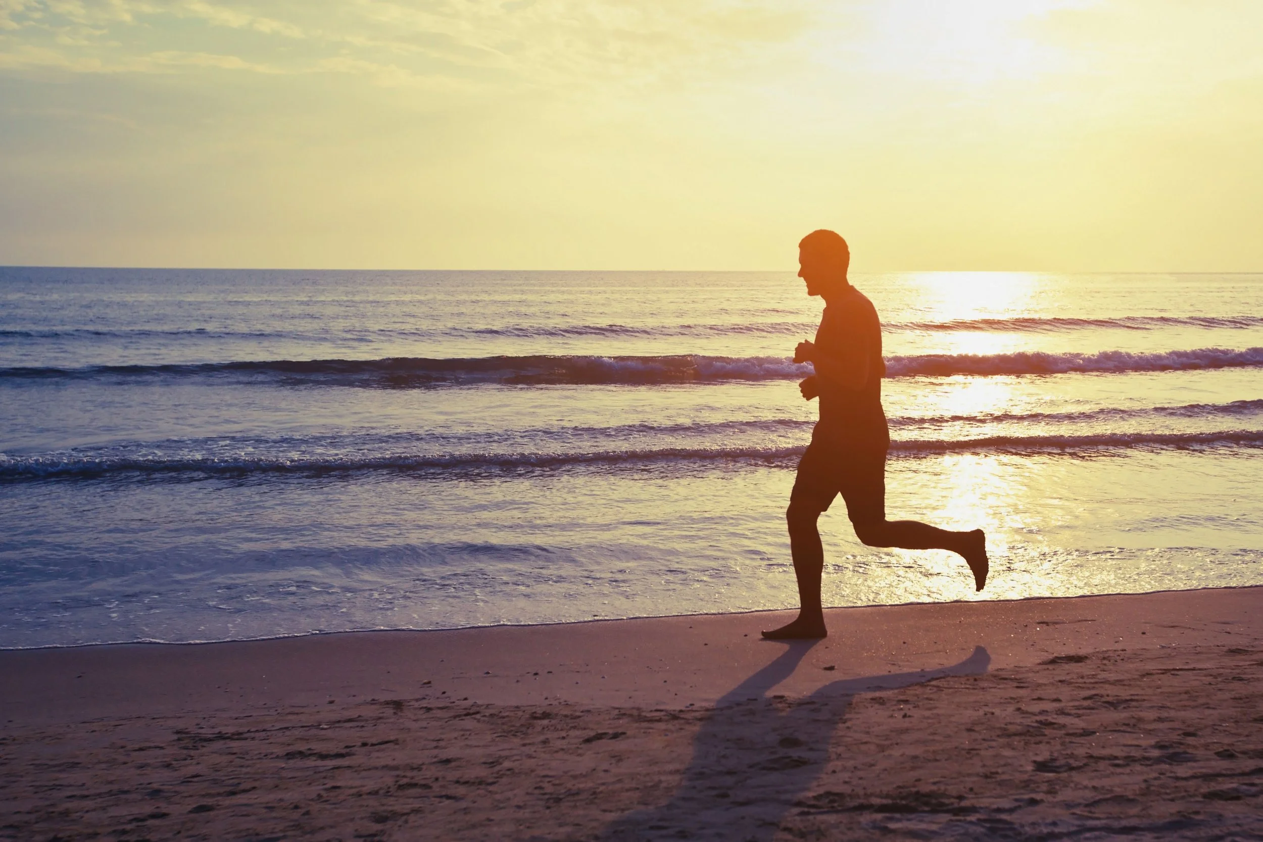 Silhouette of a man running on the beach during sunrise