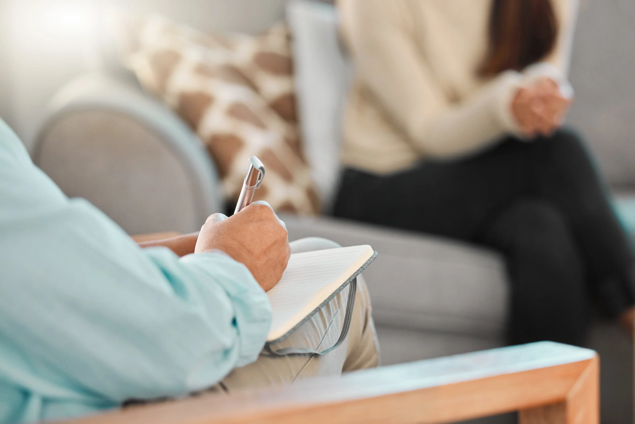 Therapist close sitting and writing with a person blurred in distance sitting.