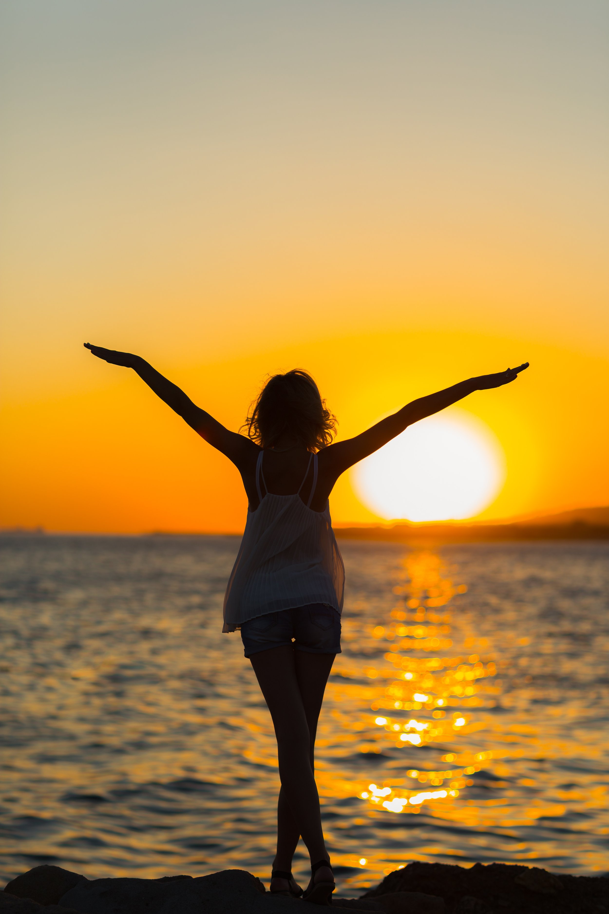 Woman with arms stretched in front of sunset on the beach.