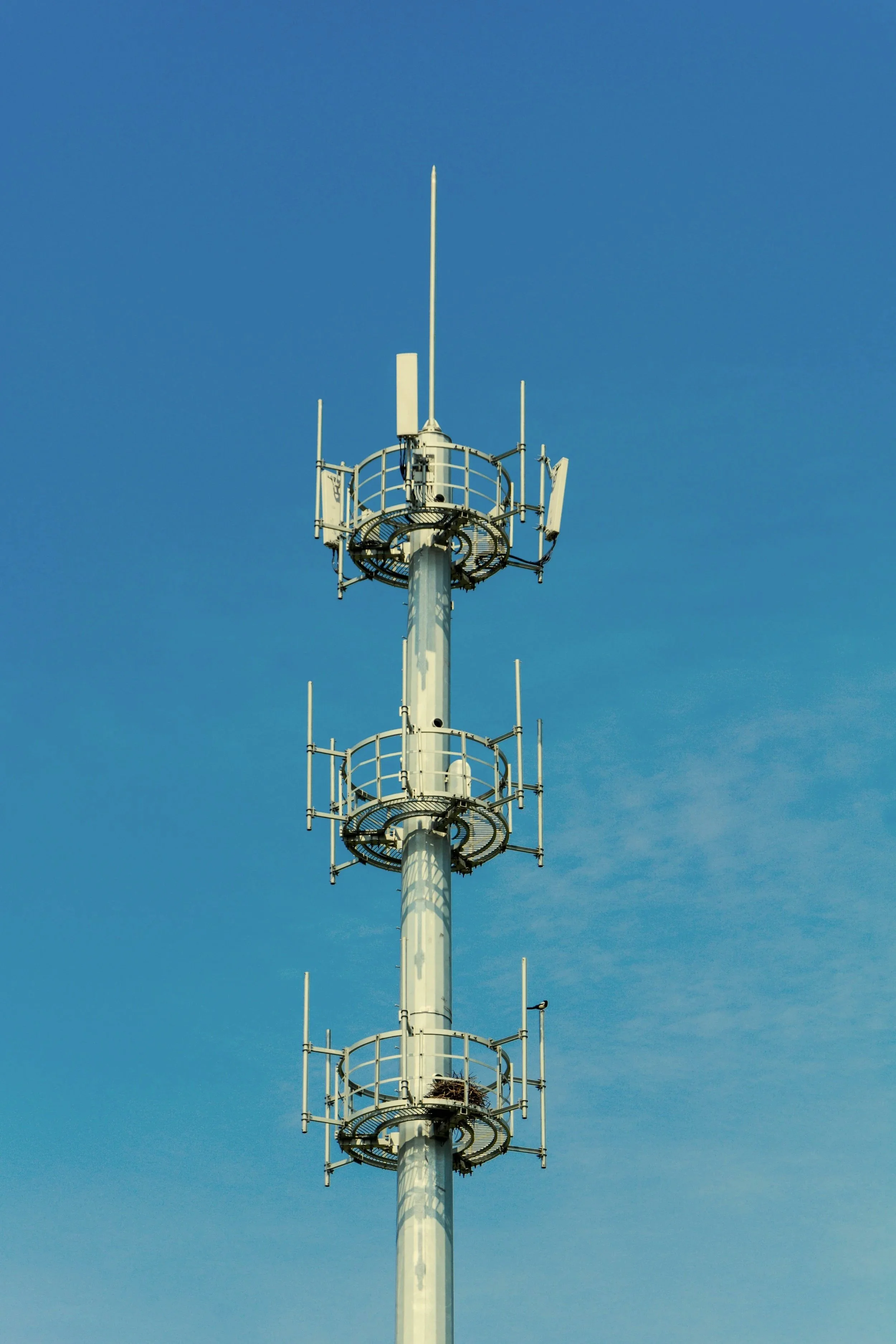 A tall telecommunications tower with multiple antennas and circular platforms, set against a clear blue sky.