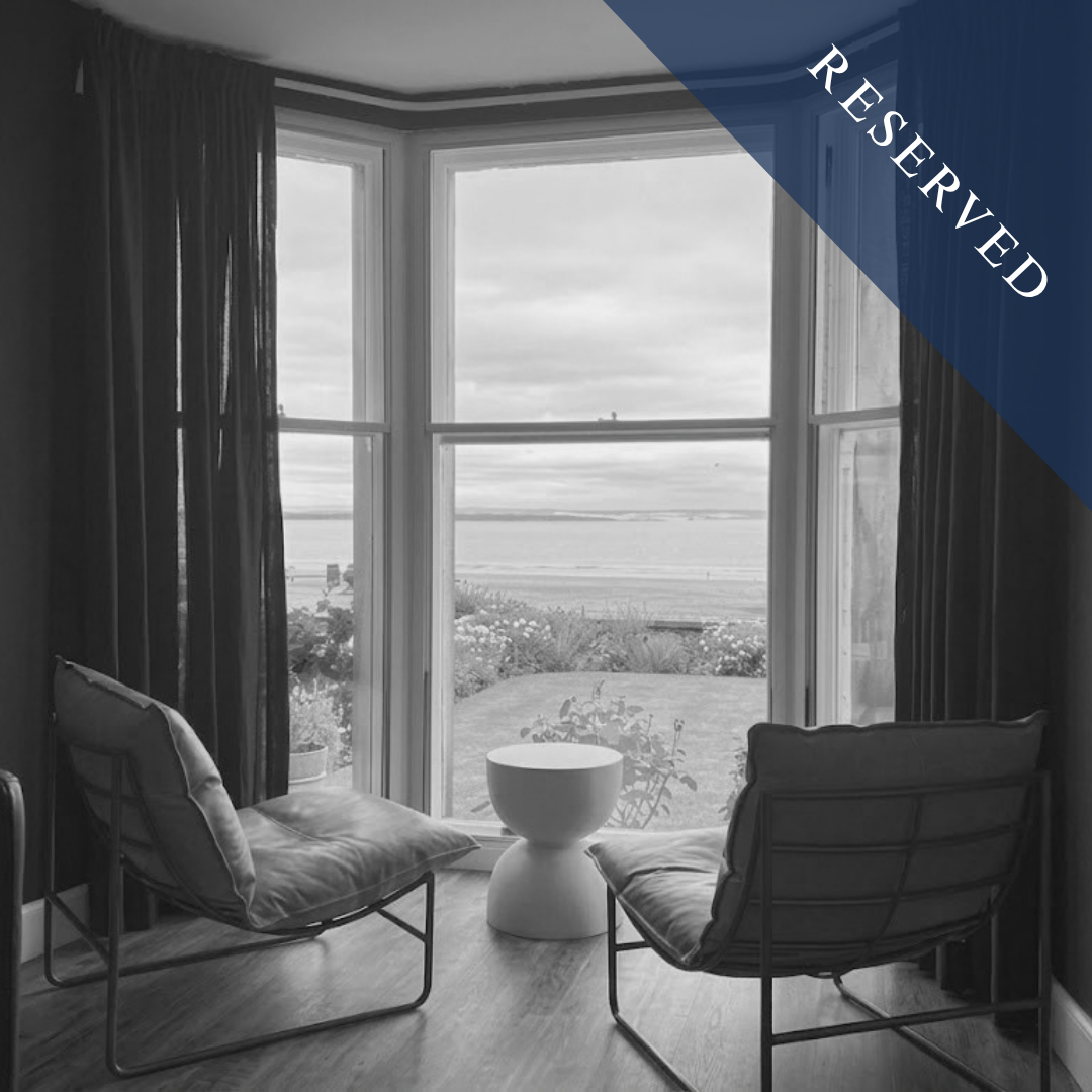 Room with two modern chairs facing a large bay window overlooking a garden and body of water, with dark curtains on each side, in black and white