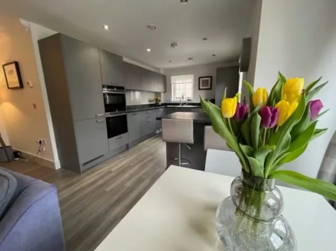 Kitchen with gray cabinets, black countertops, and a window, with a table featuring a vase of yellow and purple tulips.