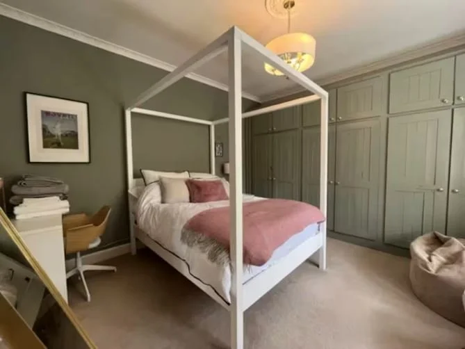 Bedroom with a white four-poster bed, pink bedding, and green built-in cabinets.