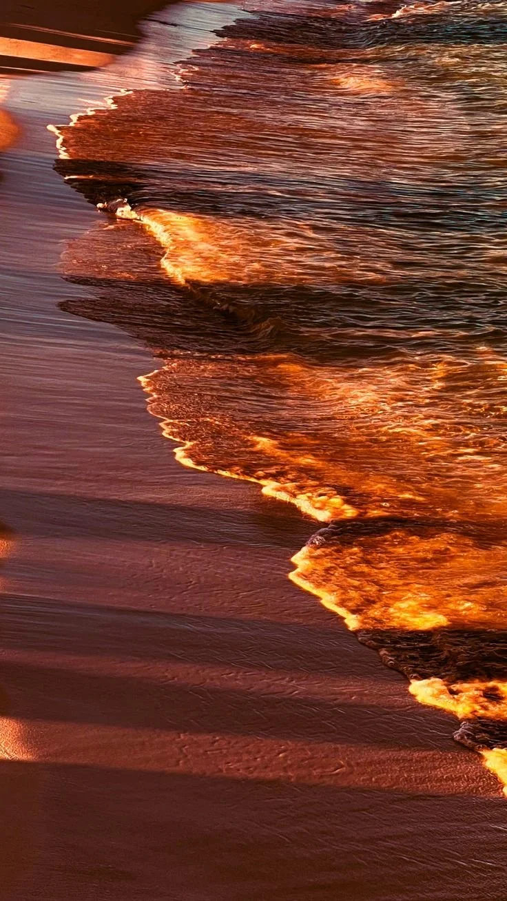 Sunset reflections on ocean waves at the beach with golden light on the water's surface.