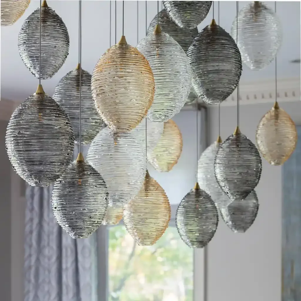 A chandelier with multiple hanging oval-shaped glass orbs in shades of clear, white, and gray, suspended from gold-colored caps.