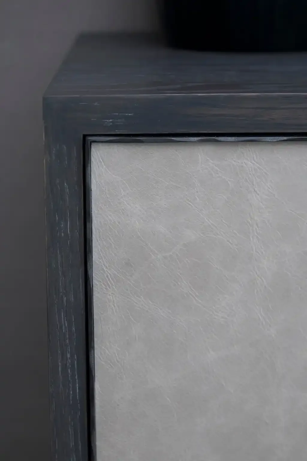 Close-up of a corner of a modern cabinet with a dark gray wood frame and white textured door.