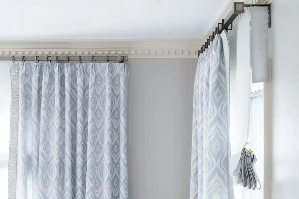 A room with white geometric patterned curtains hanging from black curtain rods on a ceiling-mounted track.