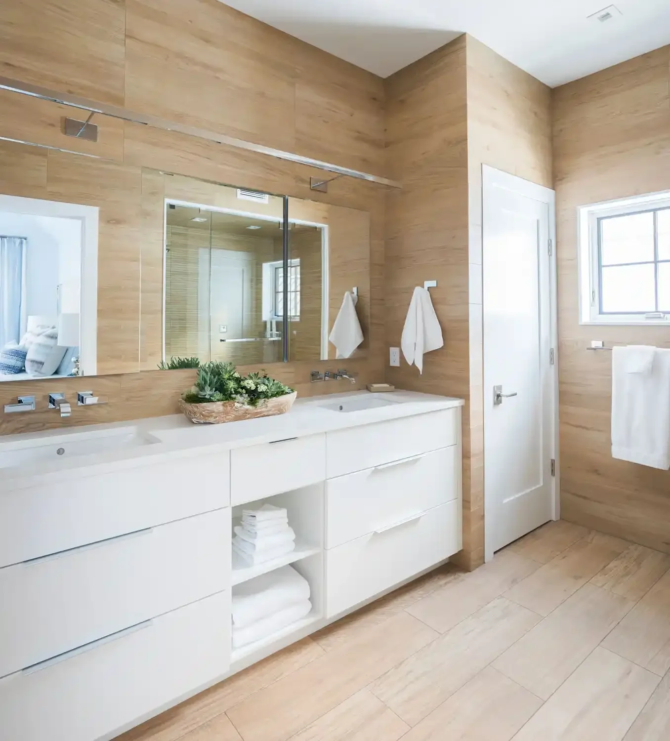 Modern bathroom with wooden walls, white vanity, large mirror, window, towels, and decorative plant.
