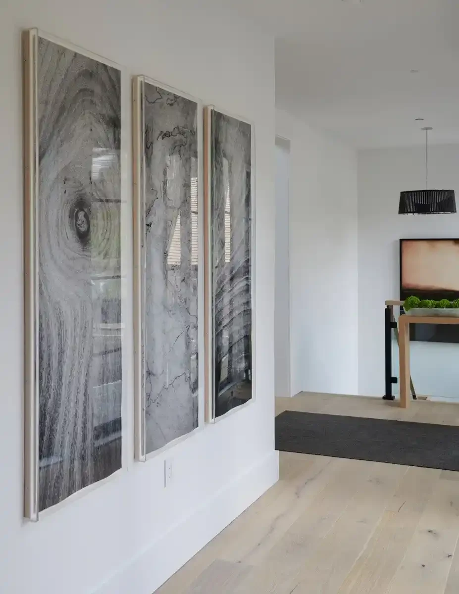 Three large abstract black and white art pieces hanging on a white wall in a modern, minimalist interior.