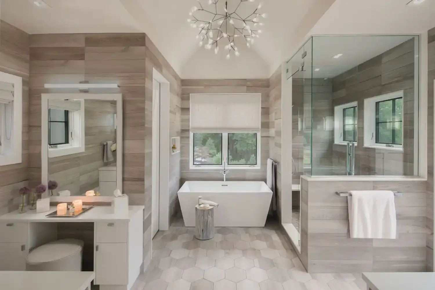 Modern bathroom with a central bathtub, hexagonal tile flooring, and a glass-enclosed shower. The walls have light wood paneling, and there are two windows providing natural light.