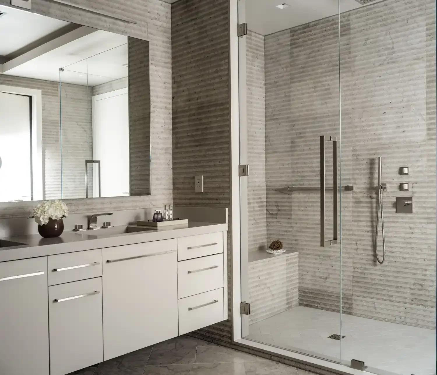 Modern bathroom with white vanity, large mirror, and glass-enclosed shower with beige tile walls and chrome fixtures.