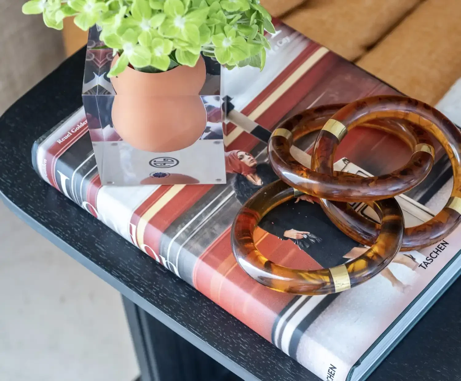 Decorative arrangement on a table including a potted plant, twisted amber-colored bangles, a magazine, and a figurine.