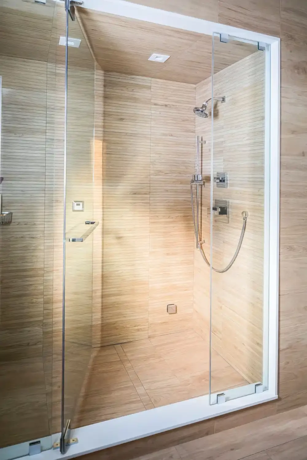 Modern walk-in shower with glass doors, wood-textured wall tiles, and metal shower fixtures.