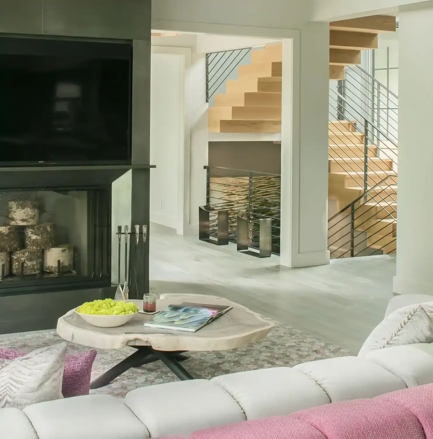 Living room with a fireplace, a TV, a coffee table with food and magazines, and a staircase with wooden steps and metal railings.