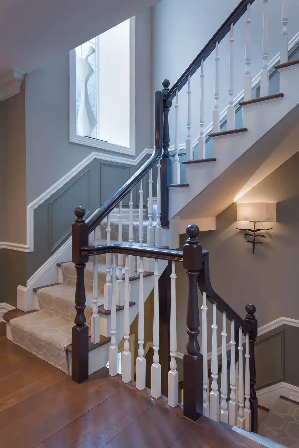 Wood staircase with white and dark wood railings, beige carpet, and wall decor, in a well-lit interior.
