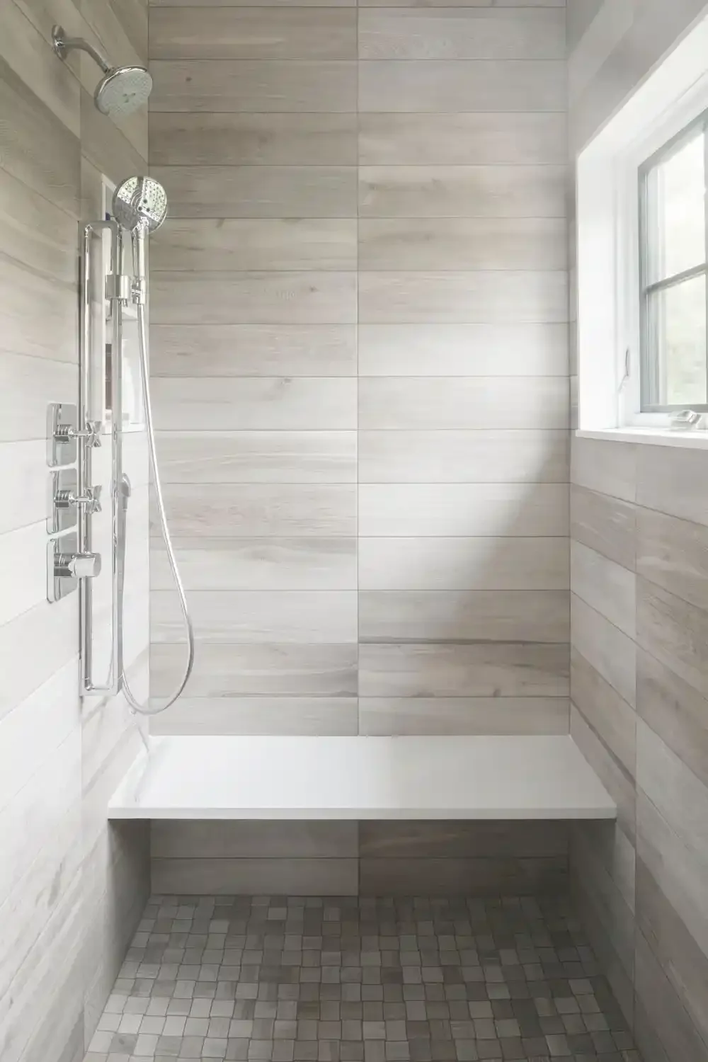 Empty walk-in shower with beige tile walls, a built-in bench, a window, and a multi-function shower with a handheld and overhead spray.
