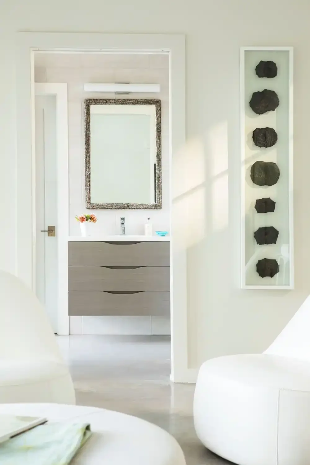 Modern bathroom with a gray vanity, framed mirror, and decorative black stones on a white wall