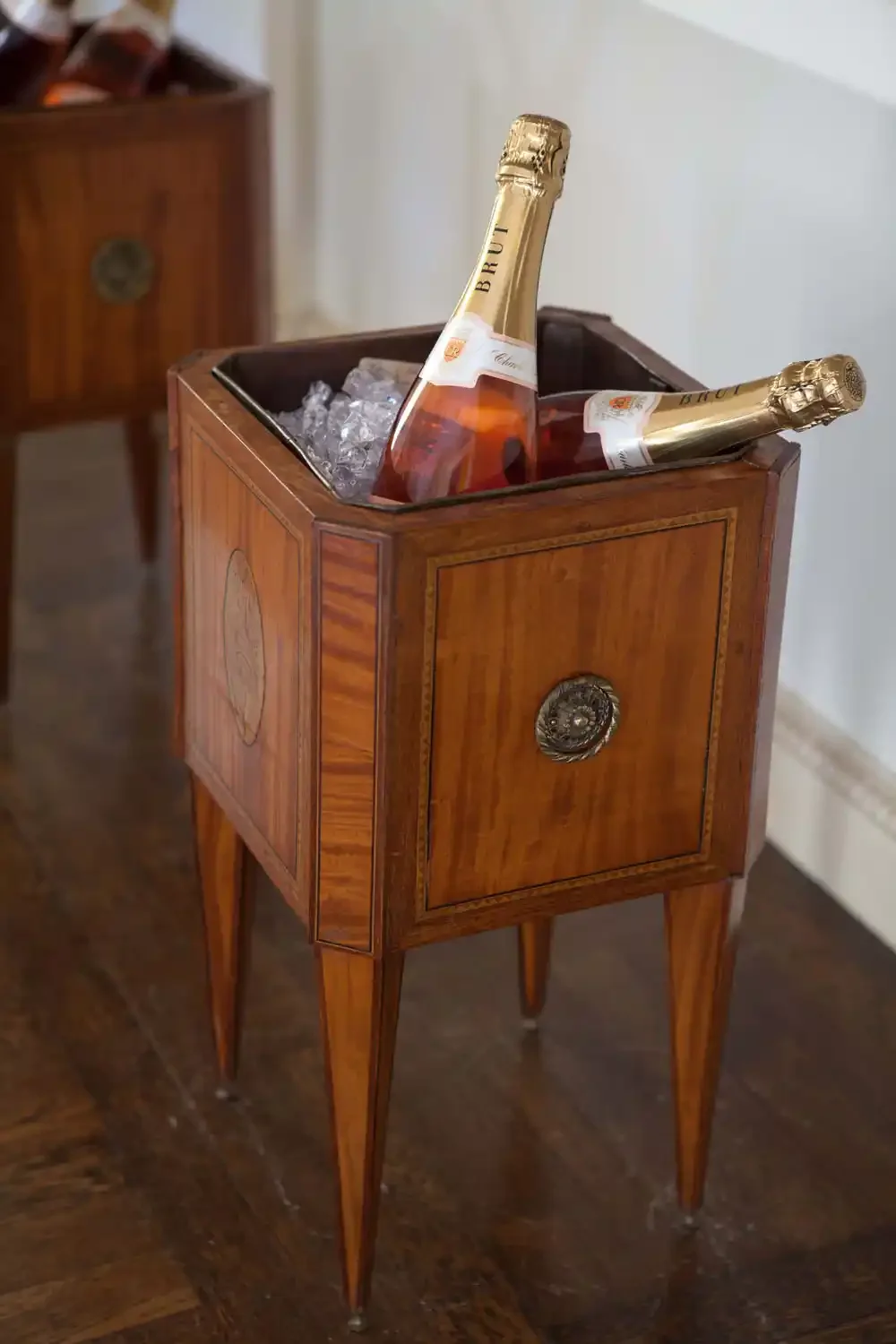 Two bottles of champagne in a wooden ice bucket filled with ice, placed on a vintage wooden side table.