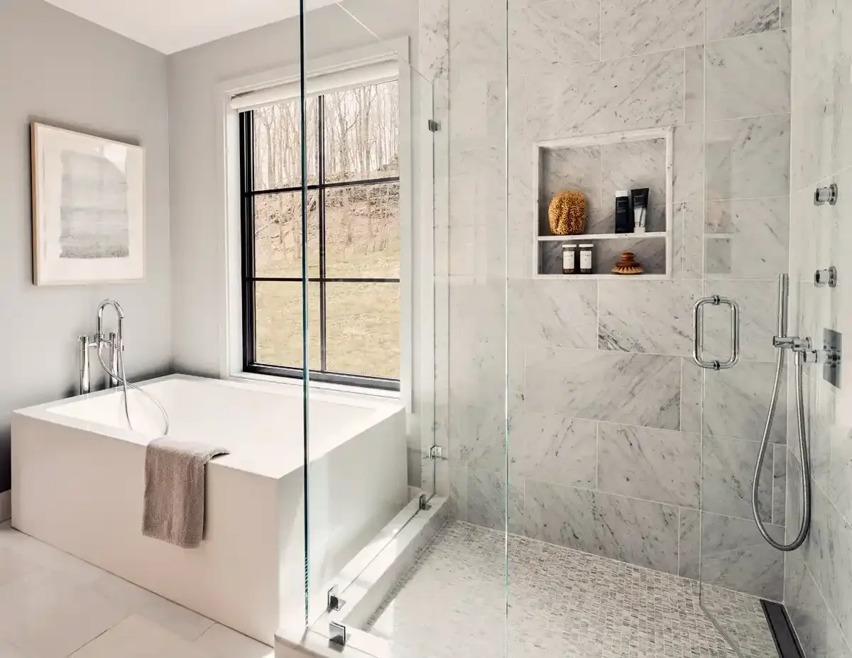 Modern bathroom with a bathtub under a large window and a separate walk-in shower with marble walls and built-in shelves.