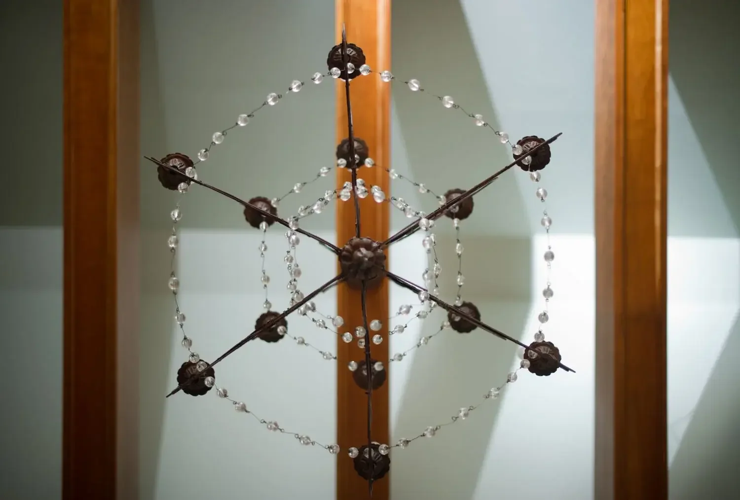 A decorative chandelier with black ornamental elements and strands of crystals, viewed from below, mounted on a wooden ceiling.