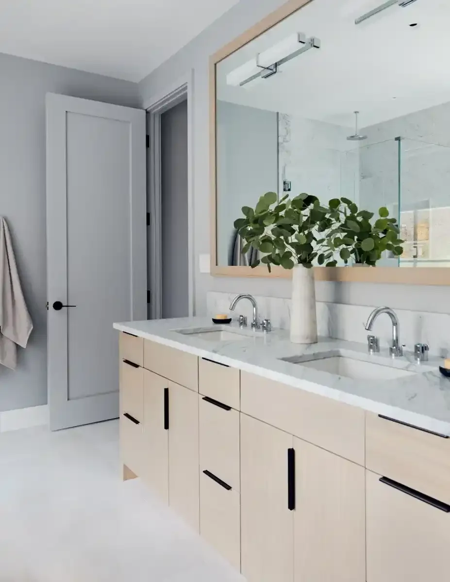 Modern bathroom with a double vanity, white marble countertop, large mirror, and green plant in a white vase.