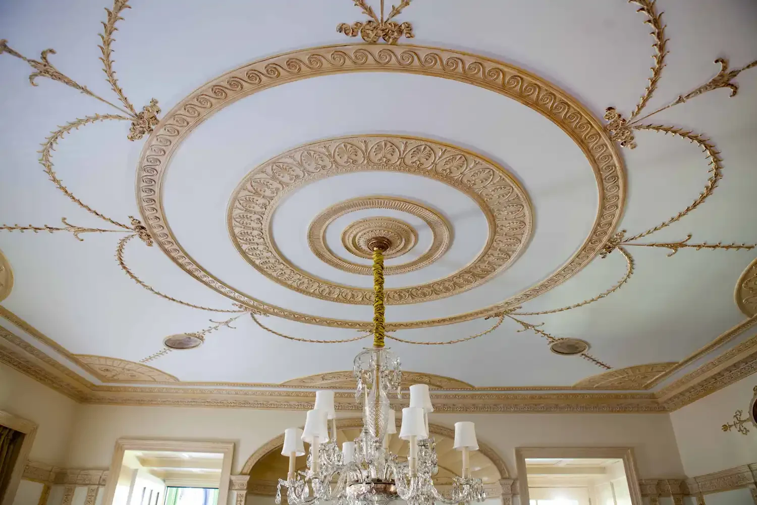 Ceiling with ornate gold detailing arranged in concentric circles, a central chandelier with multiple light fixtures, and decorative molding with gold accents.