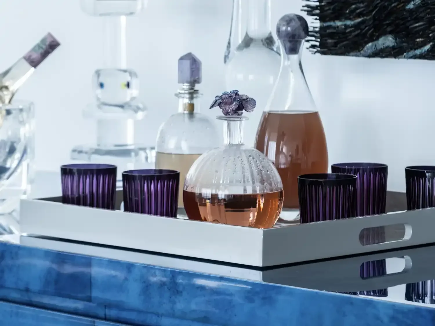 Collection of glass decanters with colored liquids and purple glasses on a white tray.